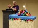 The ARRL's 100th birthday cake (actually, cupcakes were served) sparkles, as ARRL President Kay Craigie, N3KN, joins the applause in the background. [Becky Schoenfeld, W1BXY, photo]